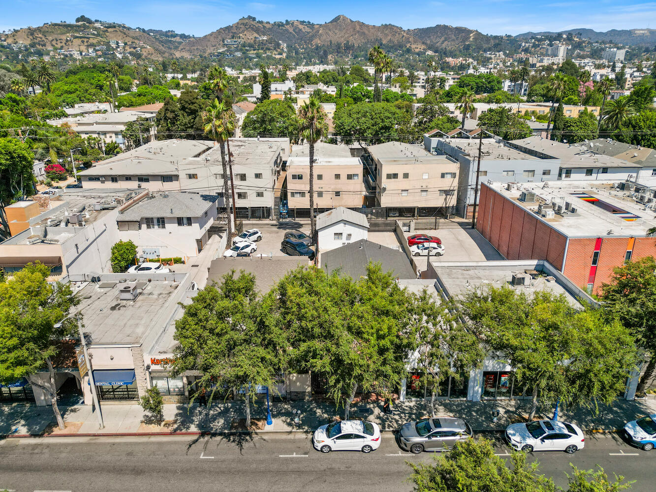 Aerial view looking north over Santa Monica Boulevard storefronts toward the Hollywood Hills and the Hollywood Sign; illustrative area photo, not a Yelena Mun listing