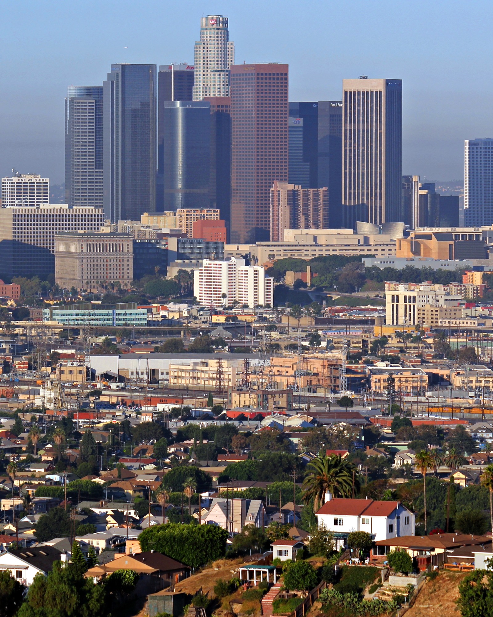 The Downtown Los Angeles skyline in warm afternoon light, seen across rooftops and hillside homes; illustrative area photo, not a Yelena Mun listing